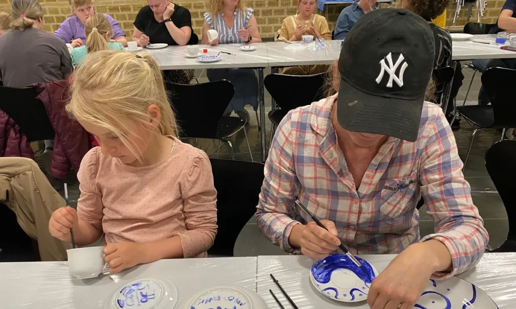 To personer maler blå mønstre på hvidt porcelæn ved workshop før teselskab i Kulturhuset
