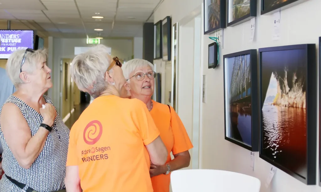 Tre kvinder fra Ældresagen studerer fotoudstillingen med naturmotiver på væg i sundhedscenter
