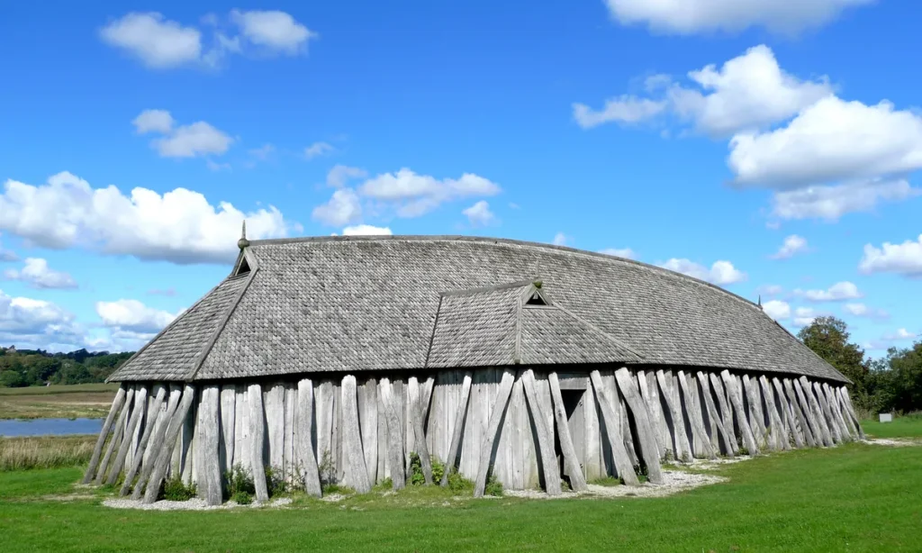 Det rekonstruerede vikingelanghus på Fyrkat med karakteristiske træplanker og stråtag under blå himmel med hvide skyer.