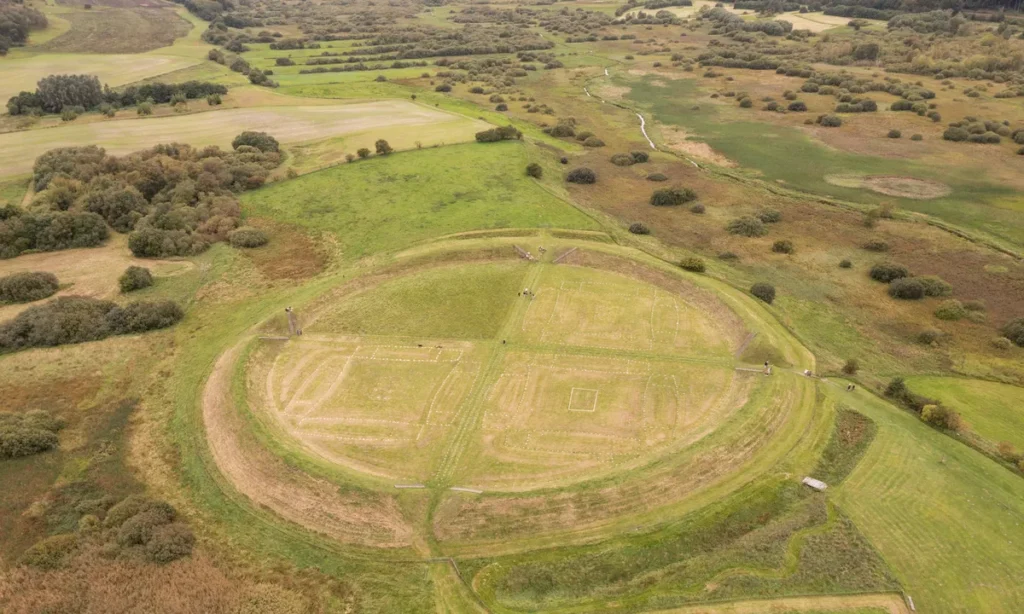 Luftfoto af Fyrkat ringborg der viser den perfekte cirkulære form med synlige fundamenter af bygninger og voldanlæg i det grønne landskab.